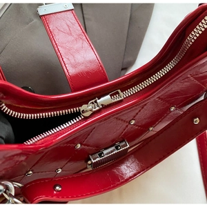 Detail of red wrinkled leather handbag featuring silver zipper and metallic rivets