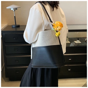 Modern black and beige patchwork bucket bag shown worn on shoulder in a minimalist interior