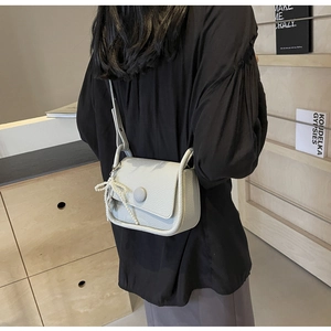 Detailed view of light gray lychee pattern saddle bag with pearl bow charm and shoulder strap