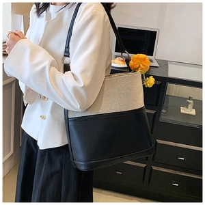 Detailed view of bicolor canvas and black leather tote bag worn by a model in office