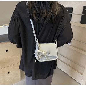 Detail view of light grey litchi grain saddle bag with pearl bow and heart charm