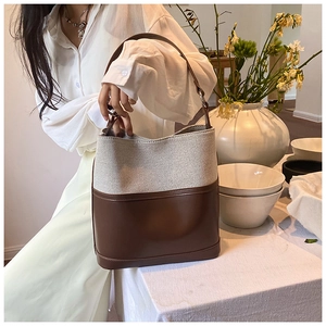 Detail of canvas bucket bag with brown leather trim on a white minimalist table