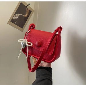Close-up of red lychee leather saddle bag with pearl bow and heart metal pendant