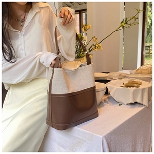 Detail of retro bucket bag in beige canvas and brown leather on an indoor table