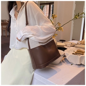 Detail of a brown leather and beige canvas bucket bag on a minimalist table scene
