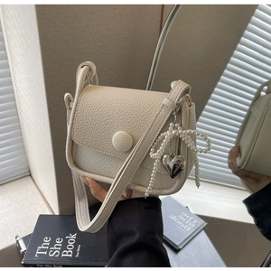 Close-up of cream lychee texture saddle bag with pearl bow and silver heart pendant detail