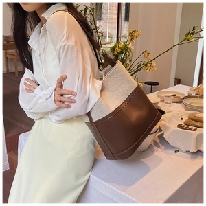 Detailed view of canvas and leather bucket bag worn by model in cozy cafe setting