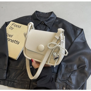 Detail of cream lychee texture saddle bag featuring pearl bow and silver heart pendant