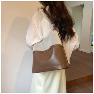 Detail view of a vintage beige canvas and brown leather bucket bag worn by a model