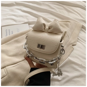Detail of cream mini box bag featuring a large bow and silver clasp on a textured surface