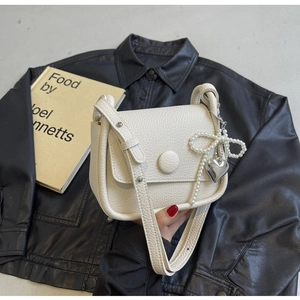 Detail of cream saddle bag with lychee texture, pearl bow and heart pendant