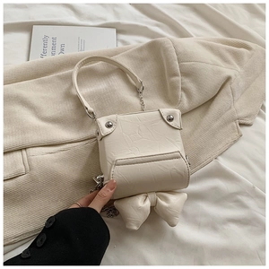 Detailed view of cream mini bow box bag with textured leather and gold chain strap