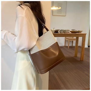 Detail of a large canvas and brown leather bucket bag in a warm indoor lifestyle setting