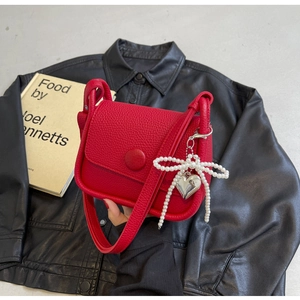 Detail of red lychee grain leather saddle bag with pearl bow and heart pendant