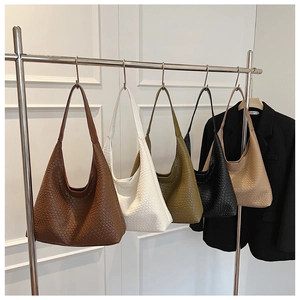 Detail of five colored woven tote bags hanging on a rack showing textured faux leather