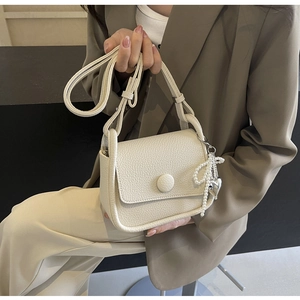 Close-up of litchi texture saddle bag with pearl bow and silver heart pendant