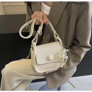 Detail of lychee pattern cream saddle bag featuring pearl bow and heart pendant