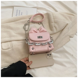 Mini pink bow crossbody bag next to a smartphone showing its compact size and shiny finish