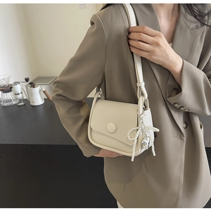 Detail of lychee textured cream saddle bag with pearl bow charm and metal heart