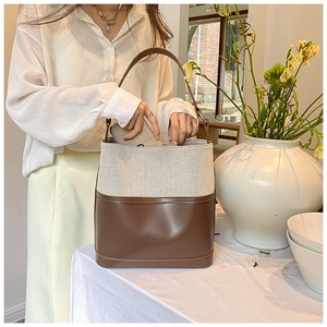 Detail of a two-tone bucket bag featuring cream canvas and dark brown leather stitching