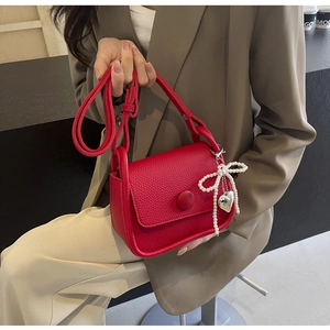 Detail of red lychee textured saddle bag with pearl bow and silver heart charm