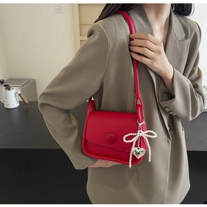 Detail of red lychee leather saddle bag with pearl bow and metal heart charm on shoulder strap