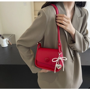 Detail of red lychee pattern saddle bag with pearl bow and heart charm on a shoulder