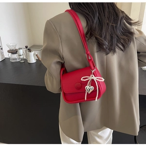 Detail of red lychee leather saddle bag with pearl bow and metal heart charm on a model