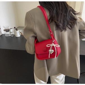 Close-up of red lychee leather saddle bag with pearl bow and silver heart pendant