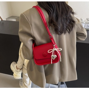 Detailed view of red saddle bag with lychee texture and pearl bow charm on a model