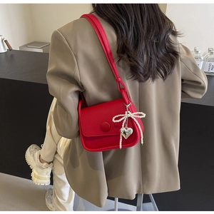 Detail of red saddle bag with lychee texture featuring pearl bow and heart metal charms