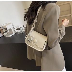 Close-up of creamy white lychee textured saddle bag with pearl bow and heart charm detail