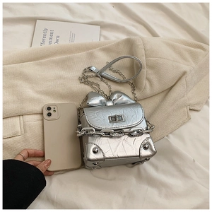Detail of silver metallic mini bag with oversized bow and punk rivet studs on white fabric