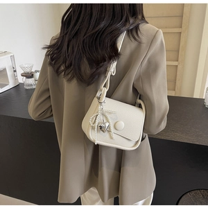 Detail of cream lychee texture saddle bag featuring pearl bow and silver heart pendant