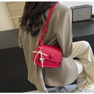 Detail of red lychee leather saddle bag with pearl bow and silver heart pendant