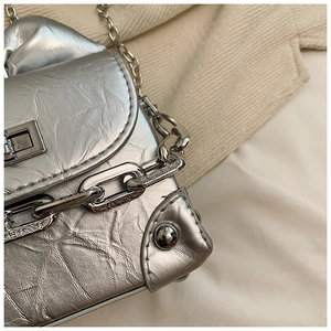 Detailed close-up of metallic silver pleated texture and engraved chain link on mini bag