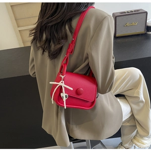 Detail of red lychee leather saddle bag with pearl and heart pendant on shoulder strap