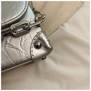 Macro detail of metallic silver bow box bag showing pleated texture and chain strap