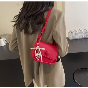 Close-up of red lychee texture saddle bag with pearl bow and silver heart pendant detail