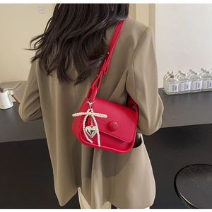 Close-up of red lychee pattern saddle bag with pearl bow and silver heart pendant