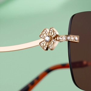 Macro detail of gold metal clover hinge with sparkling rhinestones on rimless sunglasses