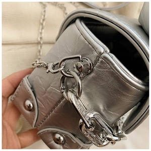 Detail of silver metallic crossbody bag featuring retro crinkled texture and punk studs