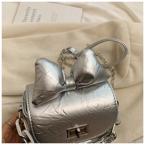 Macro detail of metallic silver bow crossbody bag featuring pleated texture and silver twist lock