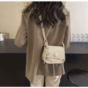 Close-up of cream lychee leather saddle bag featuring pearl bow and heart charm