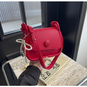 Close-up of red lychee texture saddle bag with pearl bow pendant and round buckle