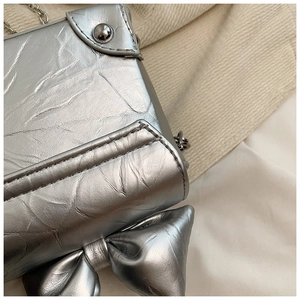 Close-up of silver mini box bag featuring a large bow and metallic pleated texture