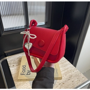 Detail of red lychee pattern leather saddle bag with pearl bow and silver heart pendant