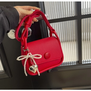 Close-up of red lychee leather saddle bag featuring pearl bow and silver heart charms
