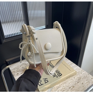 Detail of white lychee leather saddle bag with pearl butterfly charm and heart pendant