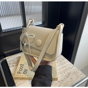 Detailed macro view of cream litchi texture saddle bag with pearl bow and heart charm